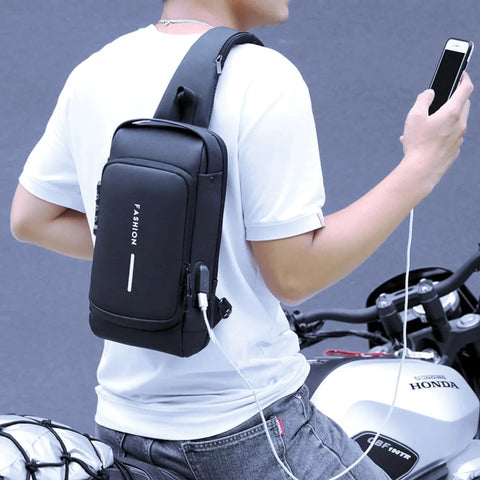 A man in a white shirt with a black "Mochila" executive fashion bag, using his phone while standing next to a motorcycle, highlighting the bag's practical USB charging port and modern style.