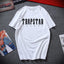 White Trapstar London T-shirt displayed on a grey textured background with magazines around, featuring a bold black Trapstar London logo on the front.