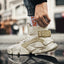 Close-up of a person wearing beige 'Exodus' unique design sneakers with chunky soles, special damping technology, and heighten design for added elevation and style, paired with rolled-up jeans and white socks with orange lettering.