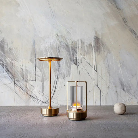 Three modern lantern-style LED lamps in different metallic finishes - silver, gold, and black - illuminating a minimalistic setting with their sleek and contemporary design.